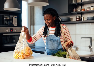 An African American Woman Is Putting Her Fresh Produce Groceries Onto The Counter Top In The Kitchen