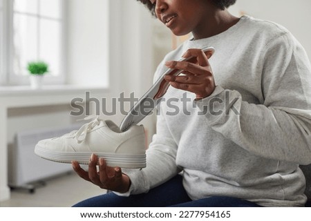 African American woman putting orthopedic insole into shoe. Close up shot of attractive woman in sweatshirt holding white leather sneaker. Foot care, prevention of flat feet and orthopedic diseases