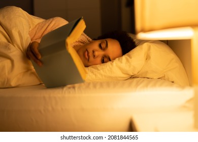 African American Woman Reading Book In Bed At Night