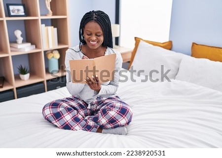 African american woman reading book sitting on bed at bedroom