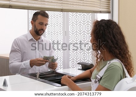 African American woman receiving money at cash department window in bank. Currency exchange