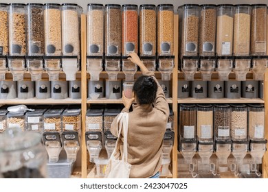 African American woman refilling reusable package with bulk products in local zero waste grocery store. Rear view - Powered by Shutterstock