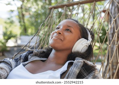 African American woman relaxing in nature on a hammock, choosing music on a smartphone and listening to favorite songs through headphones. - Powered by Shutterstock