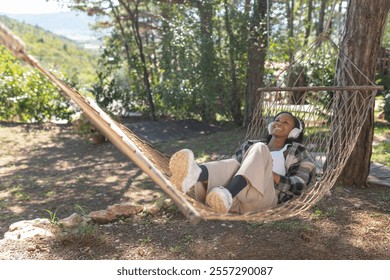 African American woman relaxing in nature on a hammock, choosing music on a smartphone and listening to favorite songs through headphones. - Powered by Shutterstock