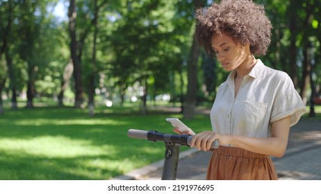 African American woman renting electric scooter via smartphone app in park - Powered by Shutterstock