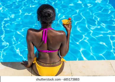 African american woman resting with cocktail near swimming pool at resort