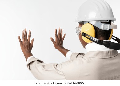 African American woman in safety gear with hard hat and ear protection, facing away, hands raised, white background. Safety gear with hard hat, ear protection, and protective eyewear on black woman. - Powered by Shutterstock