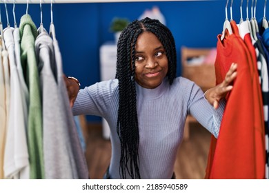 African American Woman Searching Clothes On Clothing Rack Smiling Looking To The Side And Staring Away Thinking. 