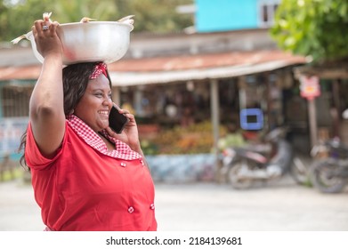 African American woman selling fish walks down the street happy talking on her cell phone.