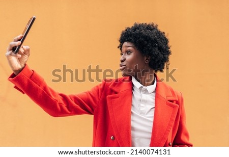 African american woman sends air kiss while taking a selfie with a mobile phone outdoors. Technology and networking concept.