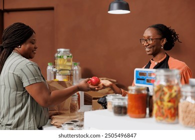 African American woman shopkeeper helps a customer at the checkout counter of a food market. Fresh produce and organic products available for purchase. - Powered by Shutterstock