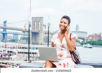 African American Woman with short afro hair traveling in New York, sitting by East River, talking on phone, working on laptop computer in same time. Manhattan, Brooklyn bridges, boat on background.
 - Shutterstock ID 1143654623