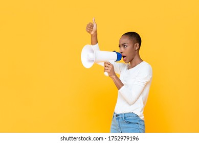African American woman shouting on megaphone and giving thumbs up isolated on yellow background