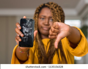 African american woman showing broken smartphone with angry face, negative sign showing dislike with thumbs down, rejection concept
