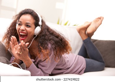 African American Woman Singing On A Sofa Wearing White Headphones