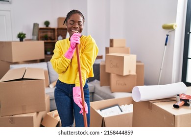 African American Woman Singing Song Using Mop As A Microphone At New Home