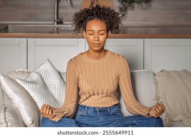 African American woman sits cross-legged on a couch, eyes closed, meditating. A peaceful moment of relaxation in a cozy home setting - Powered by Shutterstock