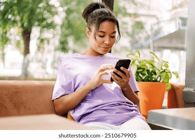 African American woman is sitting in a cafe, enjoying a moment of relaxation while using her smartphone to browse social media and connect with friends - Powered by Shutterstock