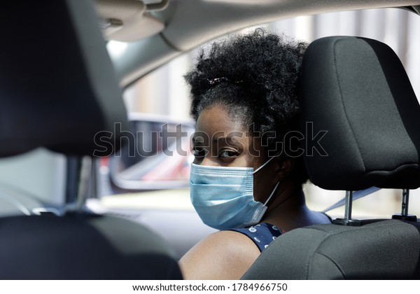African American woman sitting in car front seat\
wearing protective face\
mask