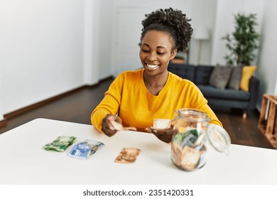 African american woman sitting on table pulling apart rand banknotes at home