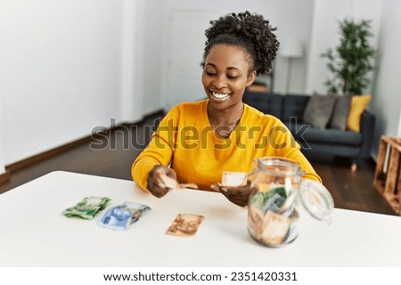 African american woman sitting on table pulling apart rand banknotes at home