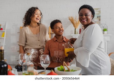 African american woman smiling at camera near daughter and grandson during thanksgiving dinner