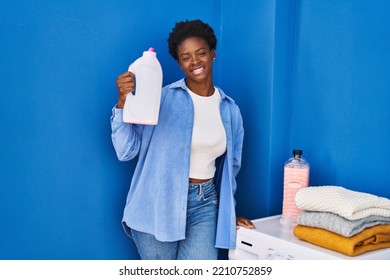 African American Woman Smiling Confident Holding Detergent Bottle At Laundry Room