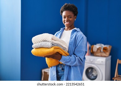 African American Woman Smiling Confident Holding Folded Clothes At Laundry Room