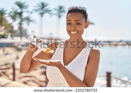 African american woman smiling confident applying sunscreen lotion at seaside