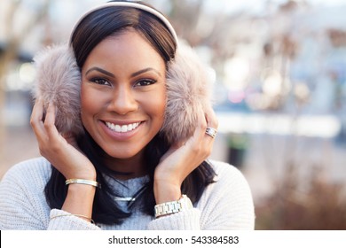 African American Woman Smiling And Grabbing Ear Muffs Downtown In The Winter Closeup