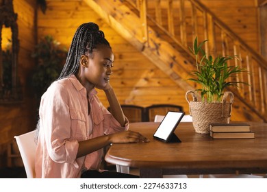 African american woman spending time in log cabin and having tablet video call with copy space. Log cabin, nature and lifestyle concept. - Powered by Shutterstock