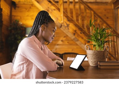 African american woman spending time in log cabin and having tablet video call with copy space. Log cabin, nature and lifestyle concept. - Powered by Shutterstock