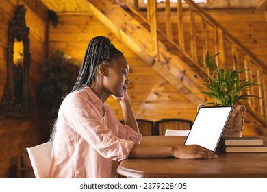 African american woman spending time in log cabin and having tablet video call with copy space. Log cabin, nature and lifestyle concept. - Powered by Shutterstock