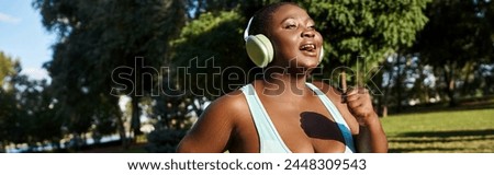 An African American woman in sportswear, with a body positive attitude, standing in a park while wearing headphones. Stock photo © 
