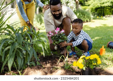 African american woman standing by father and son planting fresh flowers in field at yard. Unaltered, lifestyle, gardening, family, love, togetherness, nature and childhood concept. - Powered by Shutterstock