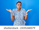 African american woman standing over blue background clueless and confused expression with arms and hands raised. doubt concept. 