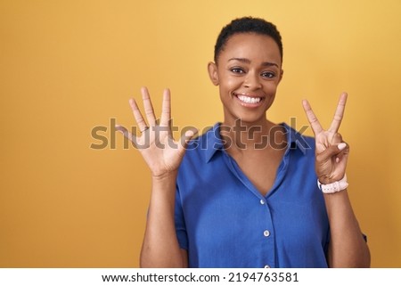 African american woman standing over yellow background showing and pointing up with fingers number seven while smiling confident and happy. 
