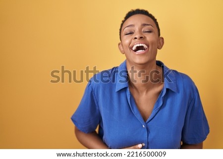 African american woman standing over yellow background smiling and laughing hard out loud because funny crazy joke with hands on body. 
