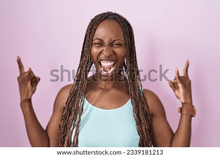 African american woman standing over pink background shouting with crazy expression doing rock symbol with hands up. music star. heavy music concept. 