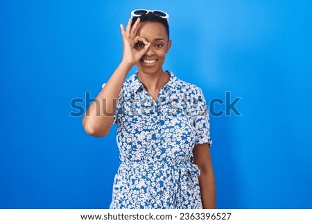 African american woman standing over blue background doing ok gesture with hand smiling, eye looking through fingers with happy face. 