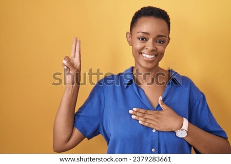 African american woman standing over yellow background smiling swearing with hand on chest and fingers up, making a loyalty promise oath 