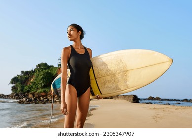 African american woman standing with surfboard on ocean beach. Black female surfer posing with surf board. Pretty multiethnic girl goes on surfing session on tropical location at sunny sunrise. - Powered by Shutterstock