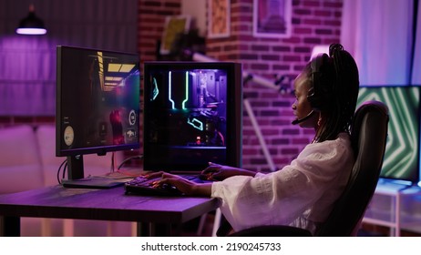 African American Woman Streaming First Person Shooter While Talking In Headset In Home Living Room. Gamer Girl Streamer Using Pc Gaming Setup Having A Good Time Playing Multiplayer Online Action