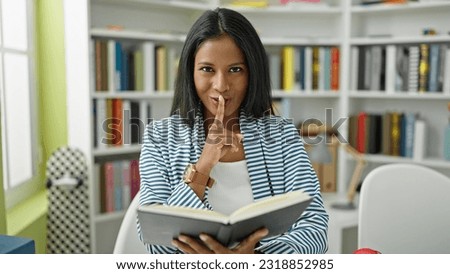 African american woman student reading book doing silence gesture at library university