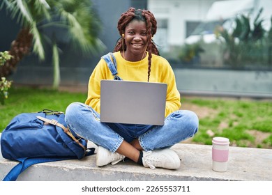 African american woman student using laptop sitting on bench at campus park - Powered by Shutterstock