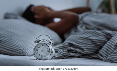 African American Woman Suffering From Insomnia Lying In Bed Without Sleep With Alarm Clocks Close Up, Panorama