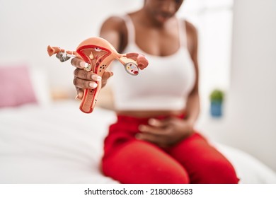 African American Woman Suffering For Menstrual Pain Holding Anatomical Model Of Uterus At Bedroom