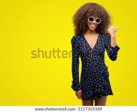 African american woman with sunglasses and summer dress pointing with hand and finger up with happy face smiling