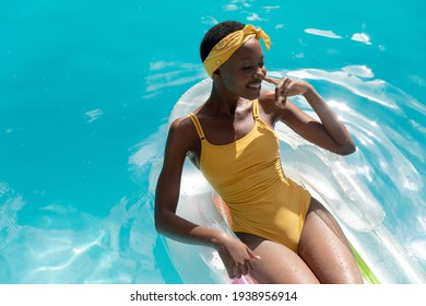 African american woman in swimming pool sunbathing on inflatable. staying at home in isolation during quarantine lockdown.