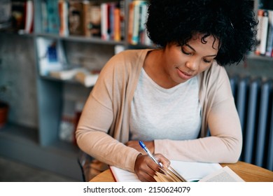 African American Woman Taking Notes While Studying At University Library. 